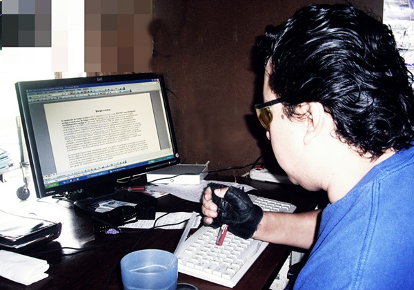 Byron Pernilla escribe en una computadora usando un guante de motociclista y un desarmador.
