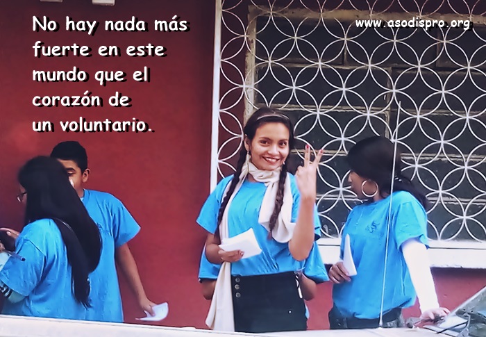 Una voluntaria de Asodispro hace la señal de la victoria sonriendo, tras de ella un grupo de voluntarios con camisas celestes conversan, sobre la fotografía un mensaje que dice: No hay nada más fuerte en este mundo que el corazón de un voluntario.