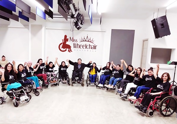 En un salón bajo reflectores, Byron Pernilla está al centro de 13 mujeres usuarias de silla de ruedas, todos se toman de las manos y las levantan.