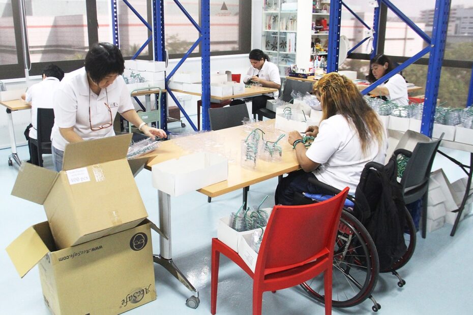 En una maquila, varias mujeres trabajan ensamblando artículos, una de ellas usuaria de silla de rueds.