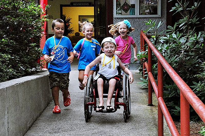 Tres niños corren tras otro niño en silla de ruedas