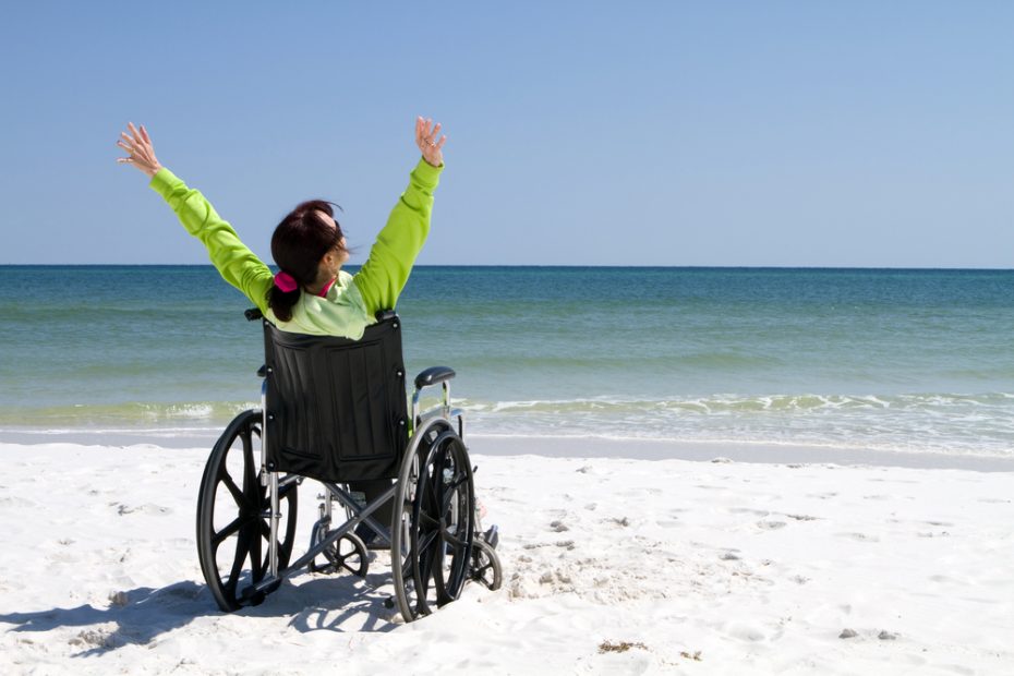 Una mujer en silla de ruedas frente al mar con los brazos extendidios.