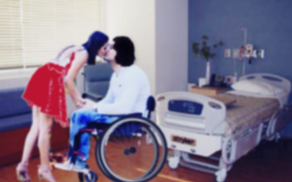 En una fotografía difusa, una chica de vestido corto rojo, besa a un chico con discapacidad de pelo largo sentado en una silla de ruedas, al fondo, se ve una cama hospitalaria.