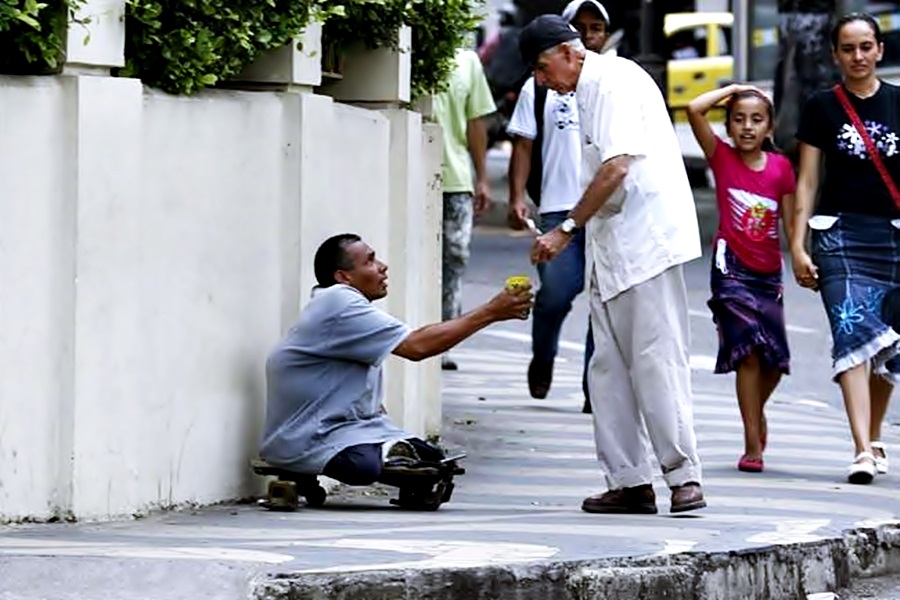 Un hombre da monedas a una persona con discapacidad