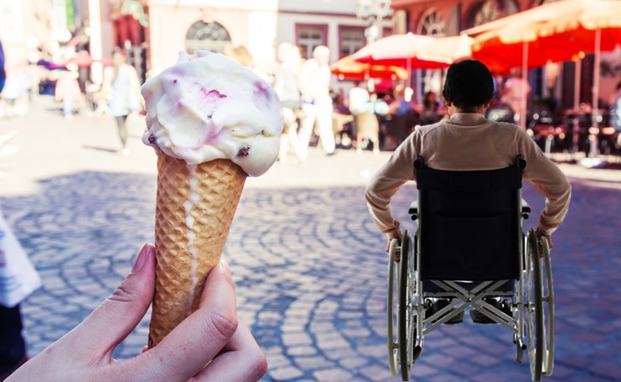 En un primer plano un helado de cono de galleta, se ve una persona de espaldas en silla de ruedas.