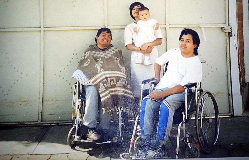En su silla de ruedas, Byron Pernilla sonríe a cámara, a su lado su esposa carga a su hijo de unos meses, junto a ellos Julio César también sonríe en su silla de ruedas