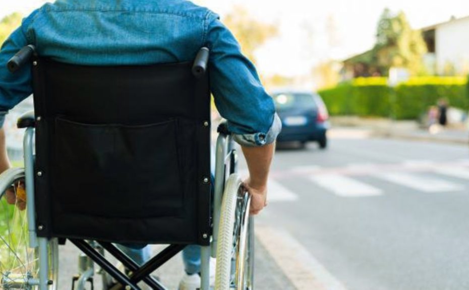 Un hombre va por la acera de una calle en silla de ruedas